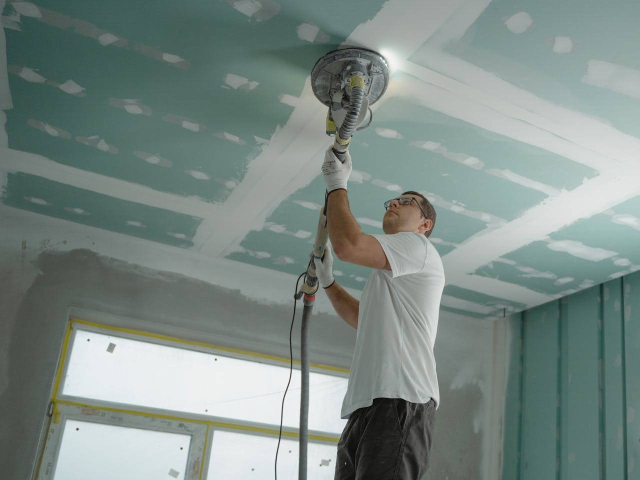 Services A professional worker sanding the ceiling during a home renovation project. Indoor construction setting.